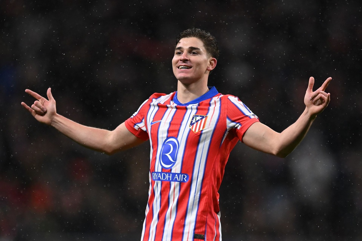 Calciatore con maglia rossa e bianca festeggia con le braccia aperte durante una partita sotto la pioggia.