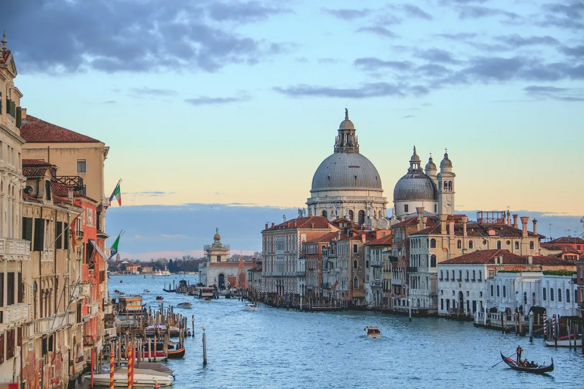 Veduta panoramica di Venezia al tramonto, con la Basilica di Santa Maria della Salute e gondole che navigano lungo il Canal Grande.