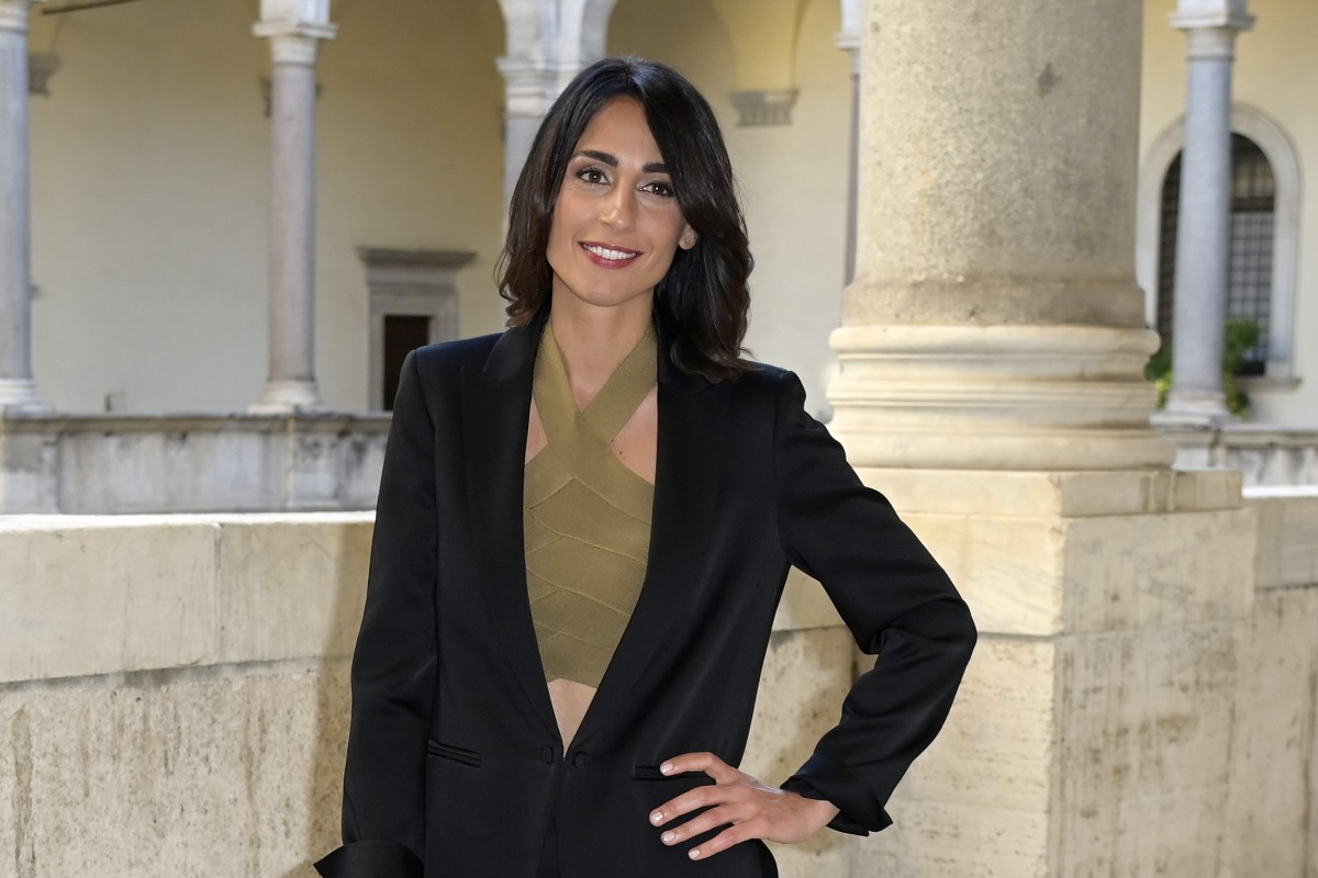 Donna elegante con tailleur nero e top incrociato verde in un cortile rinascimentale con colonne in pietra.