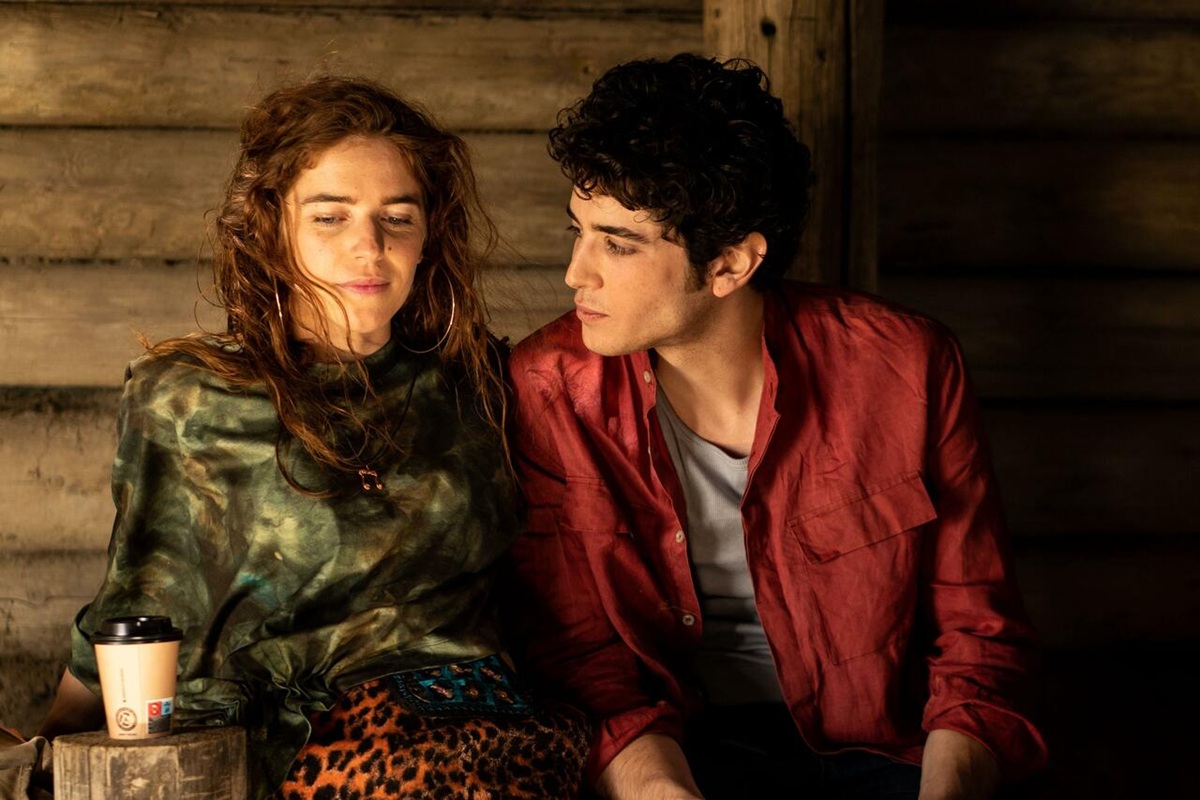 Due giovani seduti vicini in un ambiente rustico, scambio di sguardi in una scena intima e riflessiva