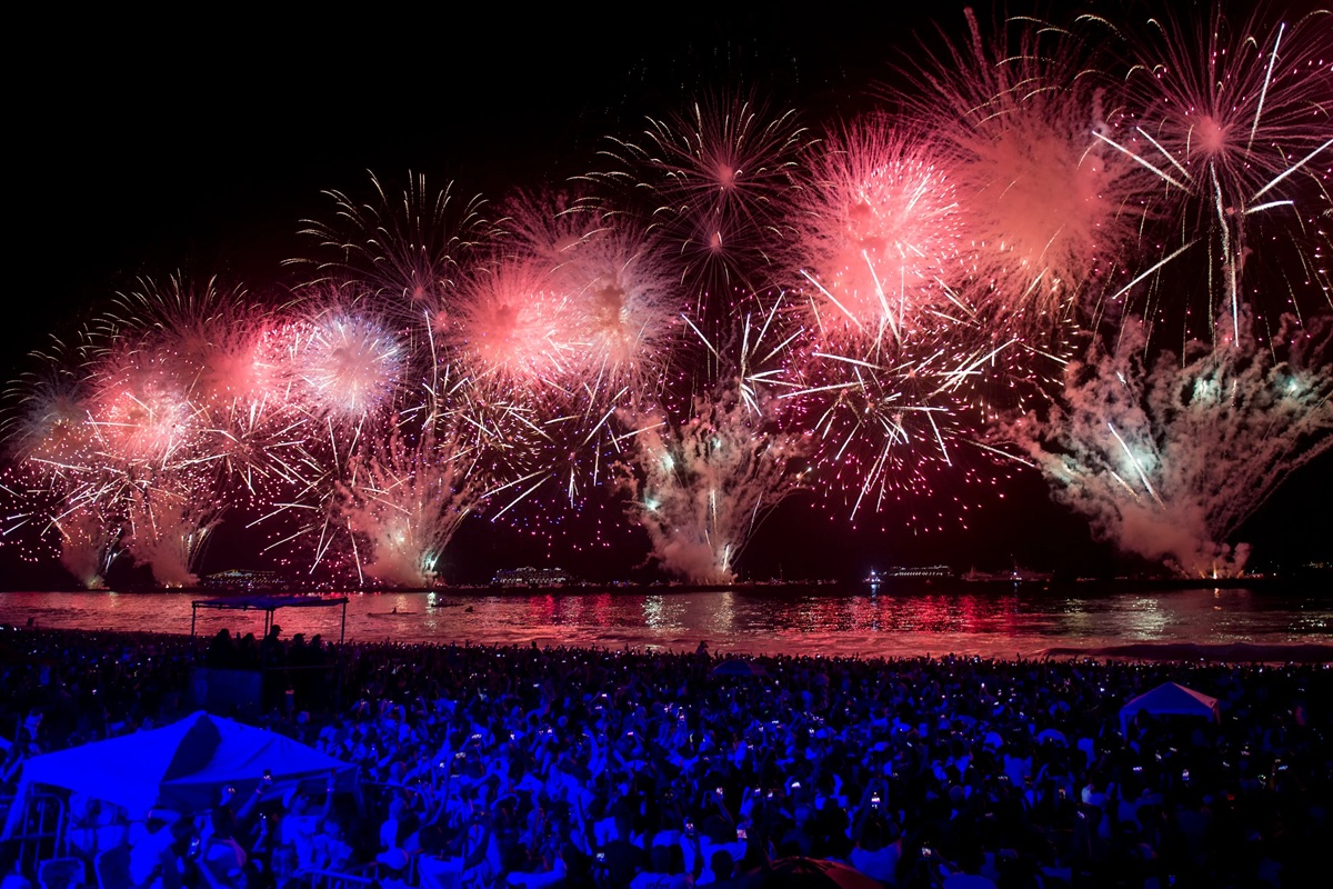 Fuochi d’artificio colorati illuminano il cielo notturno sopra il mare durante una grande celebrazione di Capodanno con folla sulla spiaggia