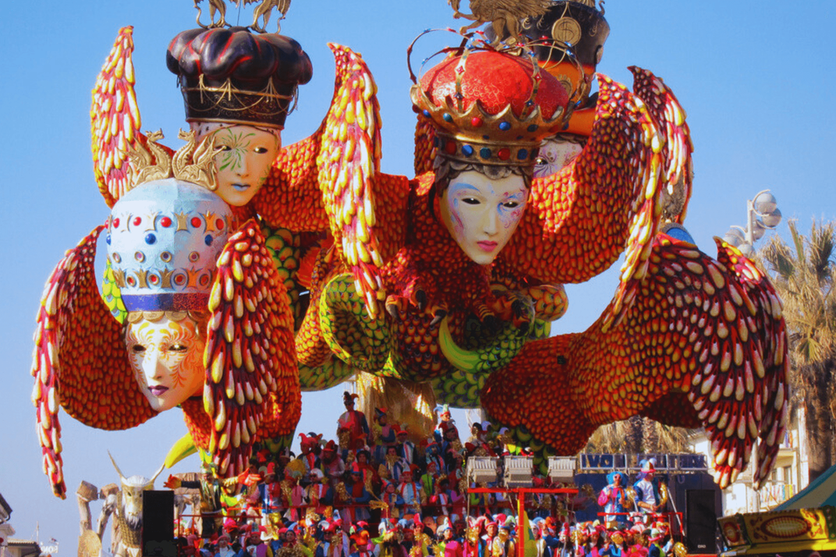 Carro allegorico del Carnevale di Viareggio con grandi maschere colorate, corone decorate e figure artistiche durante la sfilata