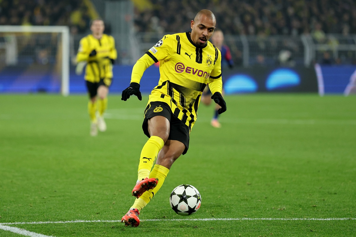 Calciatore del Borussia Dortmund in maglia gialla e nera calcia il pallone durante una partita di calcio in uno stadio illuminato