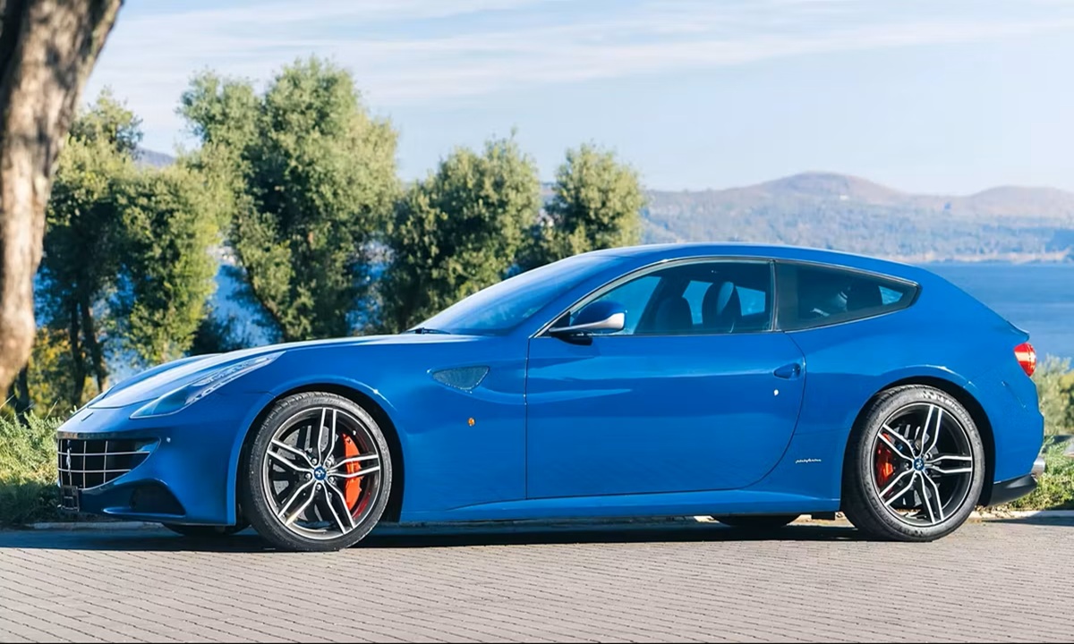 Ferrari blu vista laterale parcheggiata su strada panoramica con alberi e lago sullo sfondo