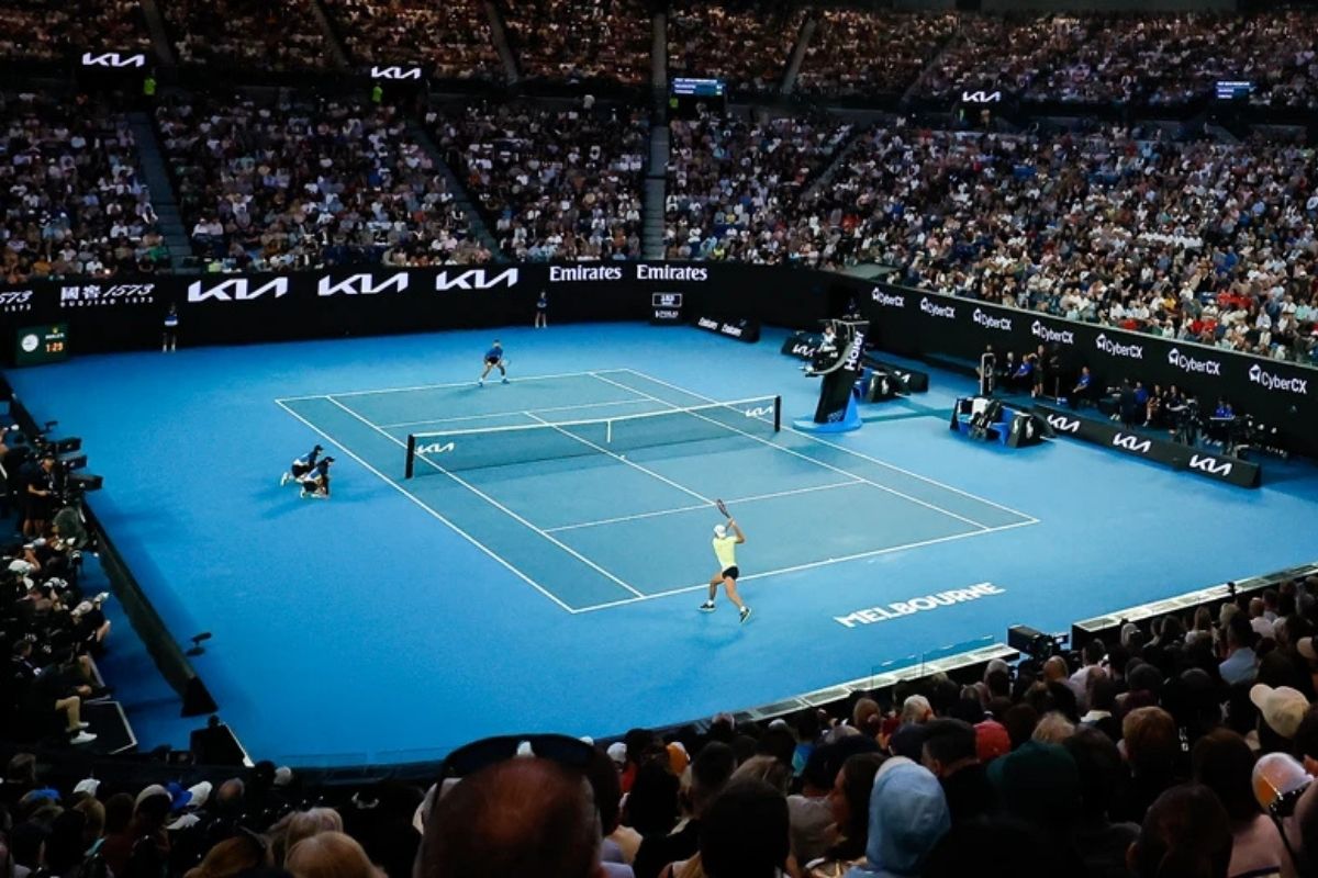 Vista panoramica di una partita di tennis su campo in cemento blu con stadio pieno di spettatori durante un torneo internazionale