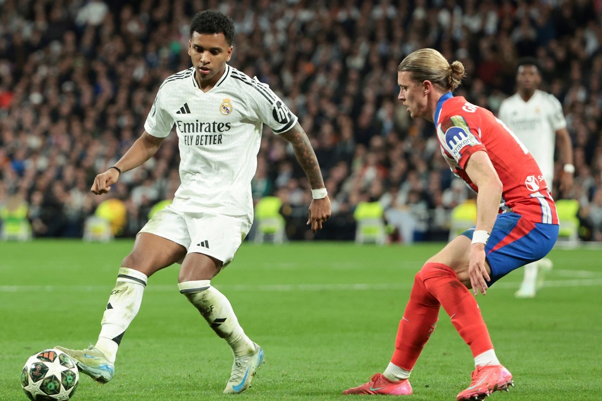 Calciatore del Real Madrid in possesso di palla affronta un avversario dell’Atlético Madrid durante una partita di calcio in uno stadio gremito.