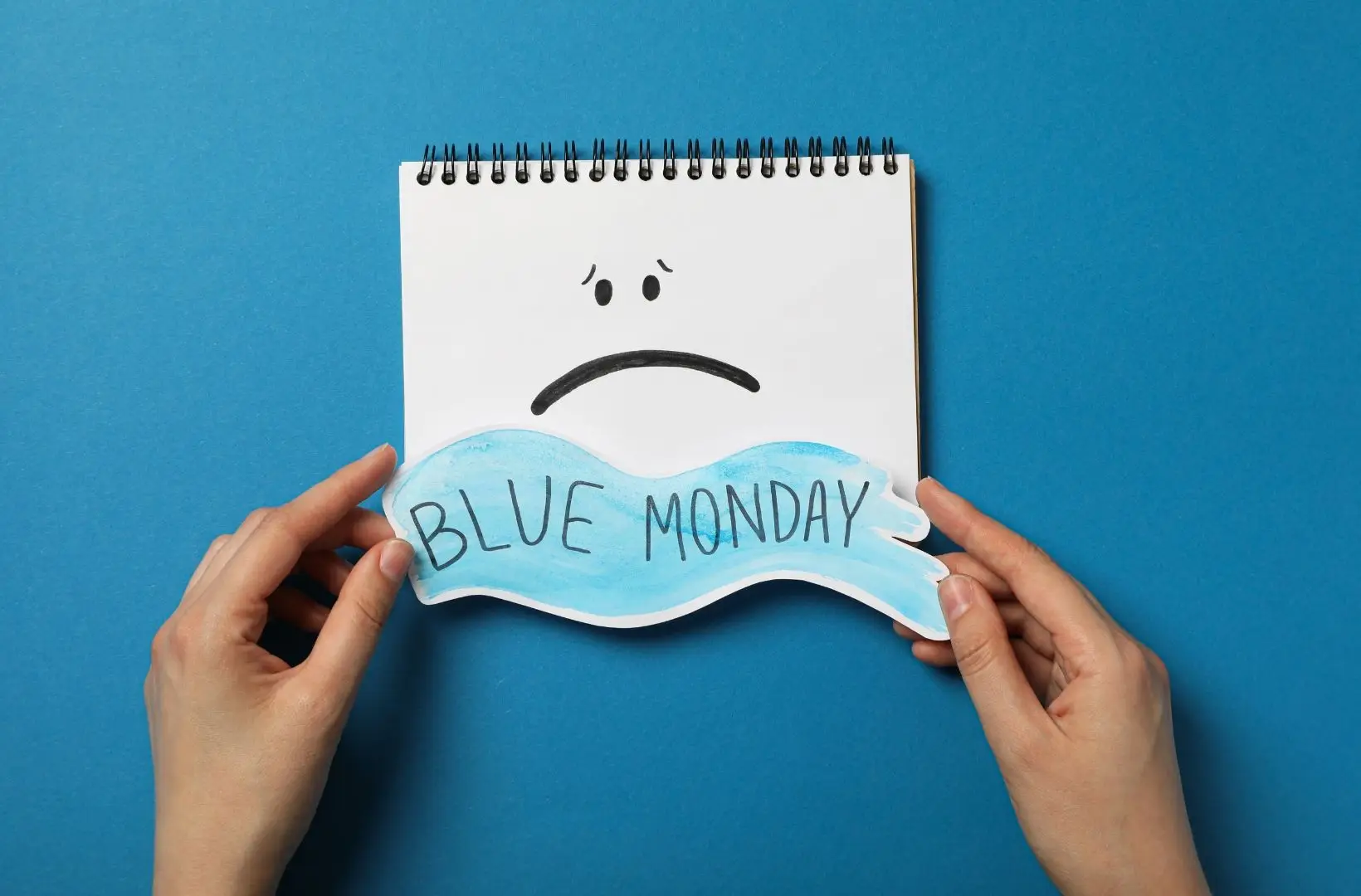 Illustrazione concettuale del Blue Monday con un taccuino che mostra un volto triste e la scritta “Blue Monday” su sfondo blu.