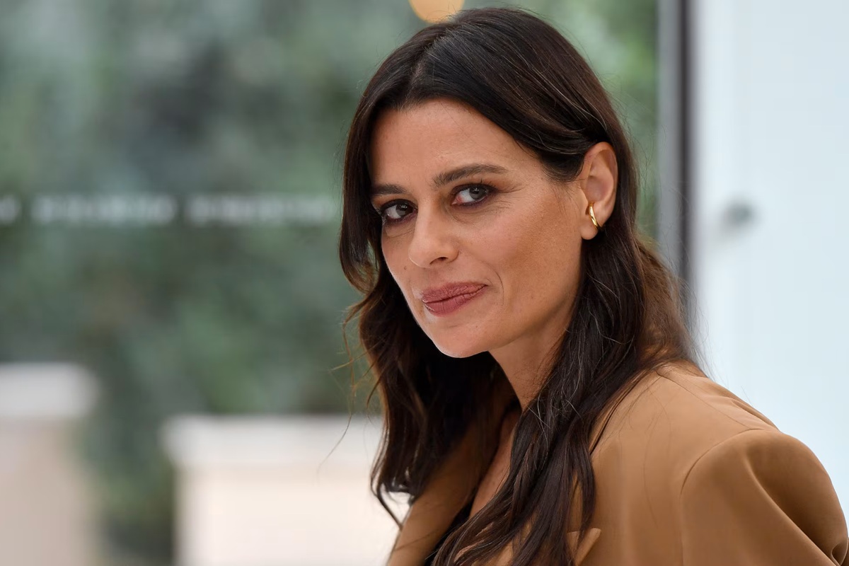 Donna dai capelli castani guarda verso la fotocamera con espressione sicura, indossando un blazer elegante in un ambiente moderno