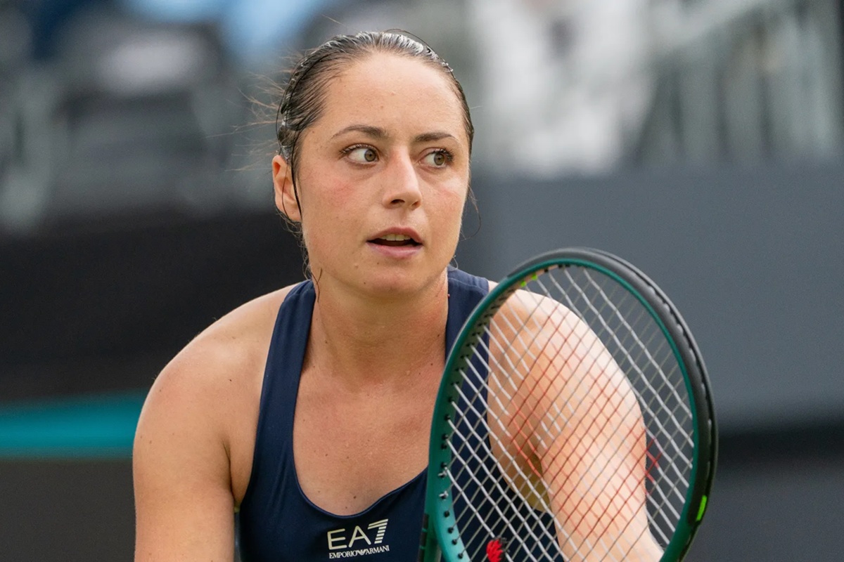 Tennista donna con racchetta in mano, espressione concentrata e abbigliamento sportivo scuro durante una partita su campo all’aperto