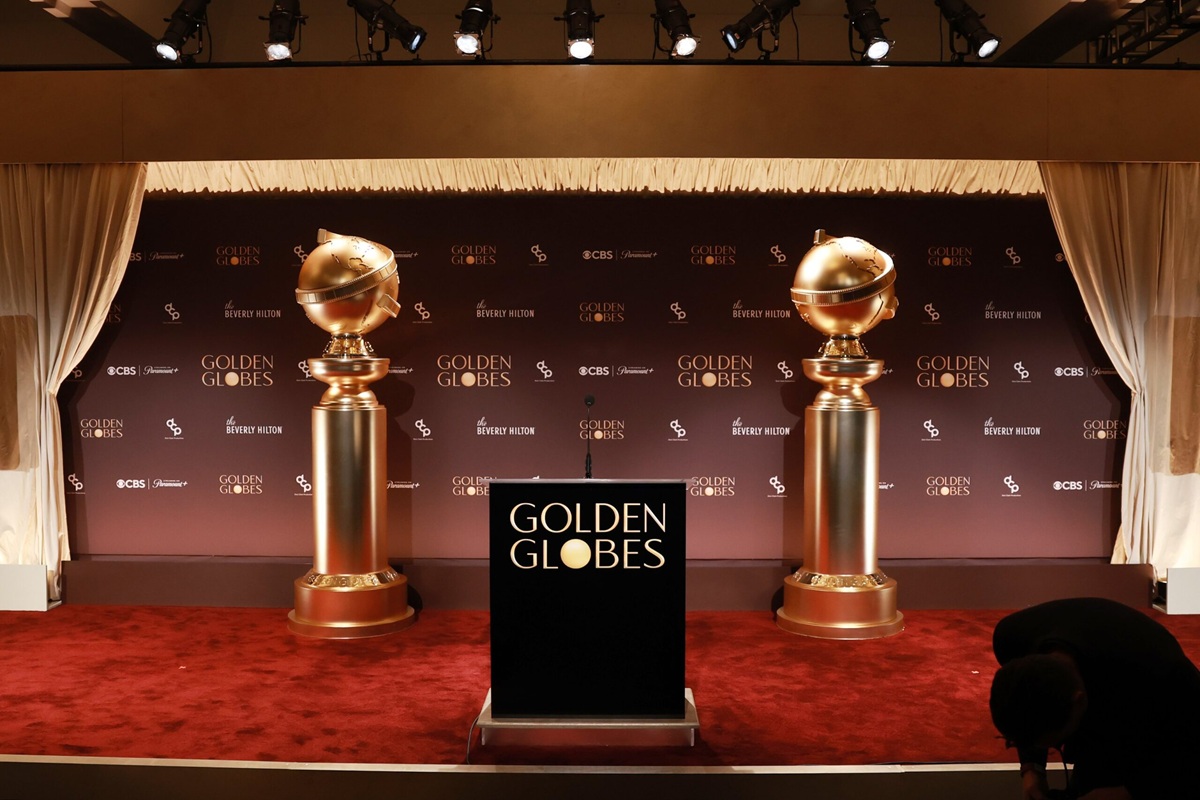 Palco dei Golden Globes con tappeto rosso, due grandi statue dorate ai lati e podio centrale con logo Golden Globes su sfondo elegante
