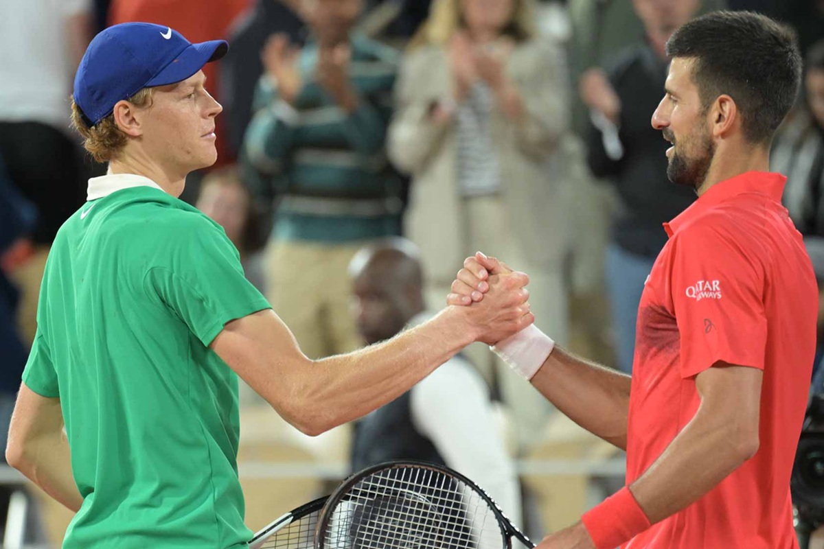 Jannik Sinner e Novak Djokovic si stringono la mano a rete dopo una partita di tennis, con il pubblico che applaude sugli spalti.