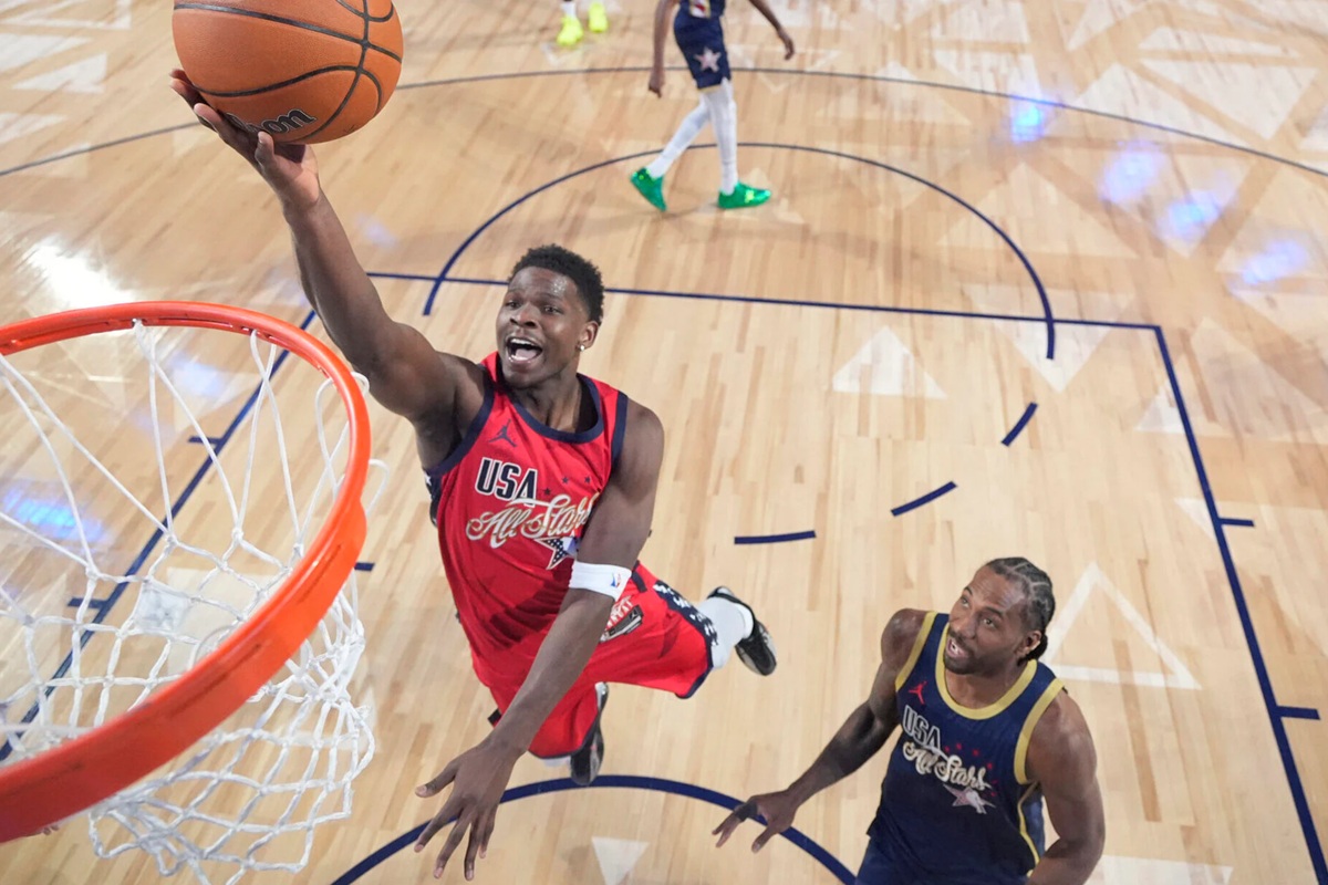 Giocatore di basket della squadra USA esegue una schiacciata durante l’NBA All-Star Game, mentre un avversario osserva sotto il canestro.