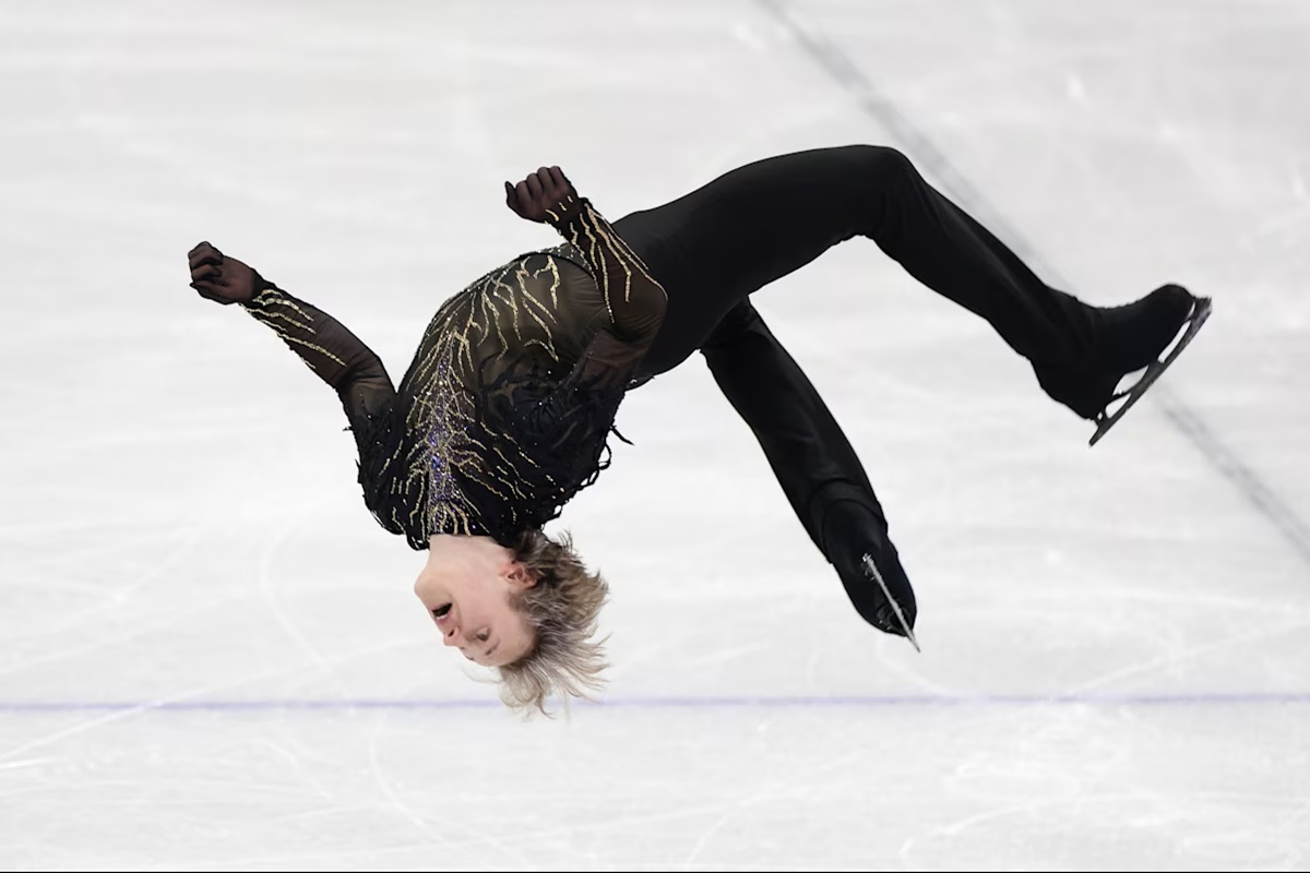 Pattinatore artistico maschile esegue un salto mortale all’indietro durante una performance alle Olimpiadi invernali su pista di ghiaccio.