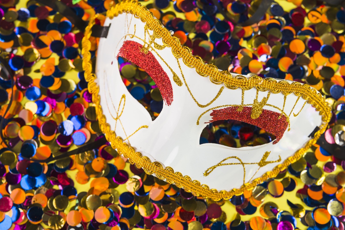 Maschera di Carnevale bianca con dettagli dorati e rossi appoggiata su coriandoli multicolore durante i festeggiamenti.