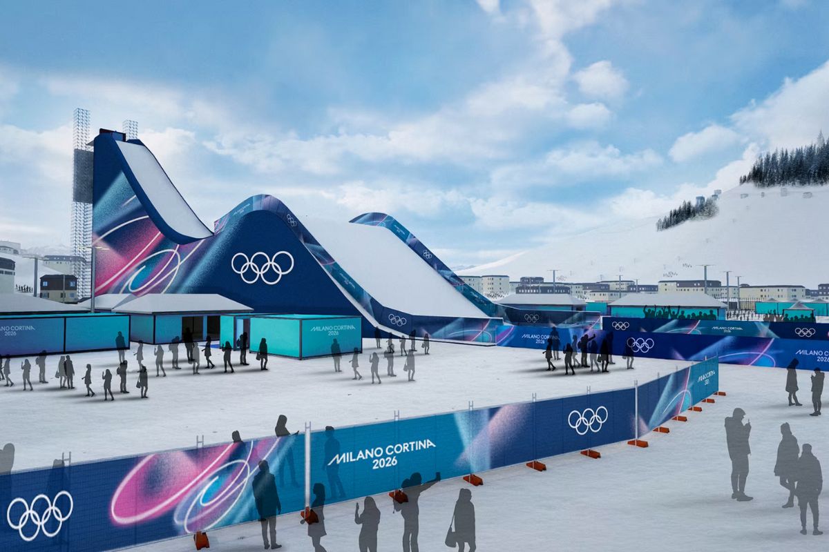 Impianto di salto con gli sci delle Olimpiadi Invernali Milano Cortina 2026, con rampe olimpiche, branding ufficiale e spettatori nell’area innevata.