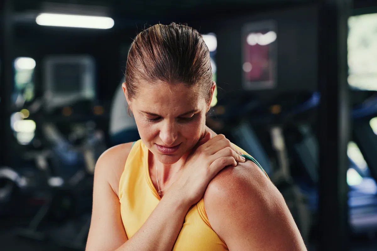 Donna in palestra che si tiene la spalla mentre mostra un fastidio muscolare dopo l'esercizio.