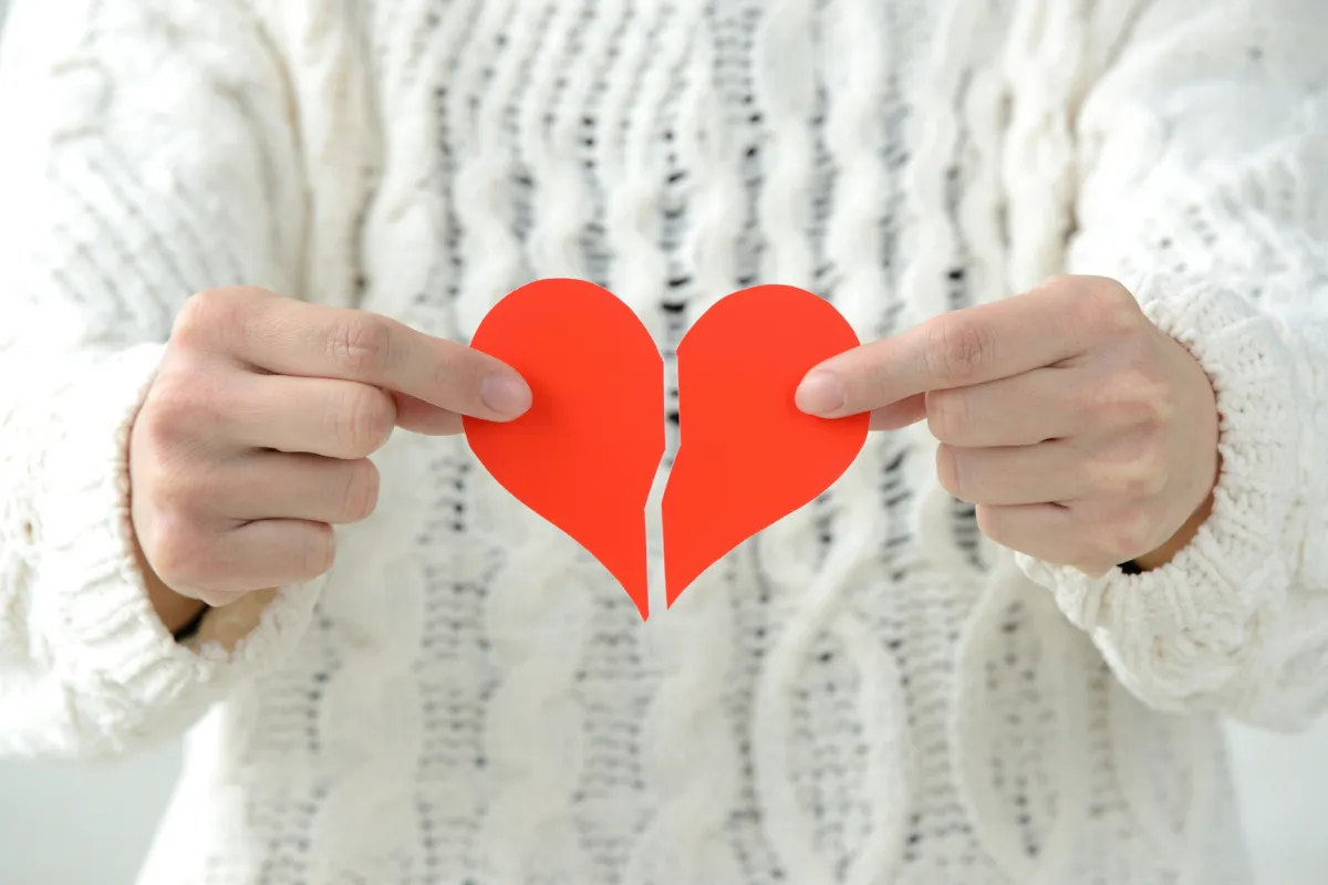 Una persona che tiene con entrambe le mani un cuore di carta rosso, spezzato a metà.