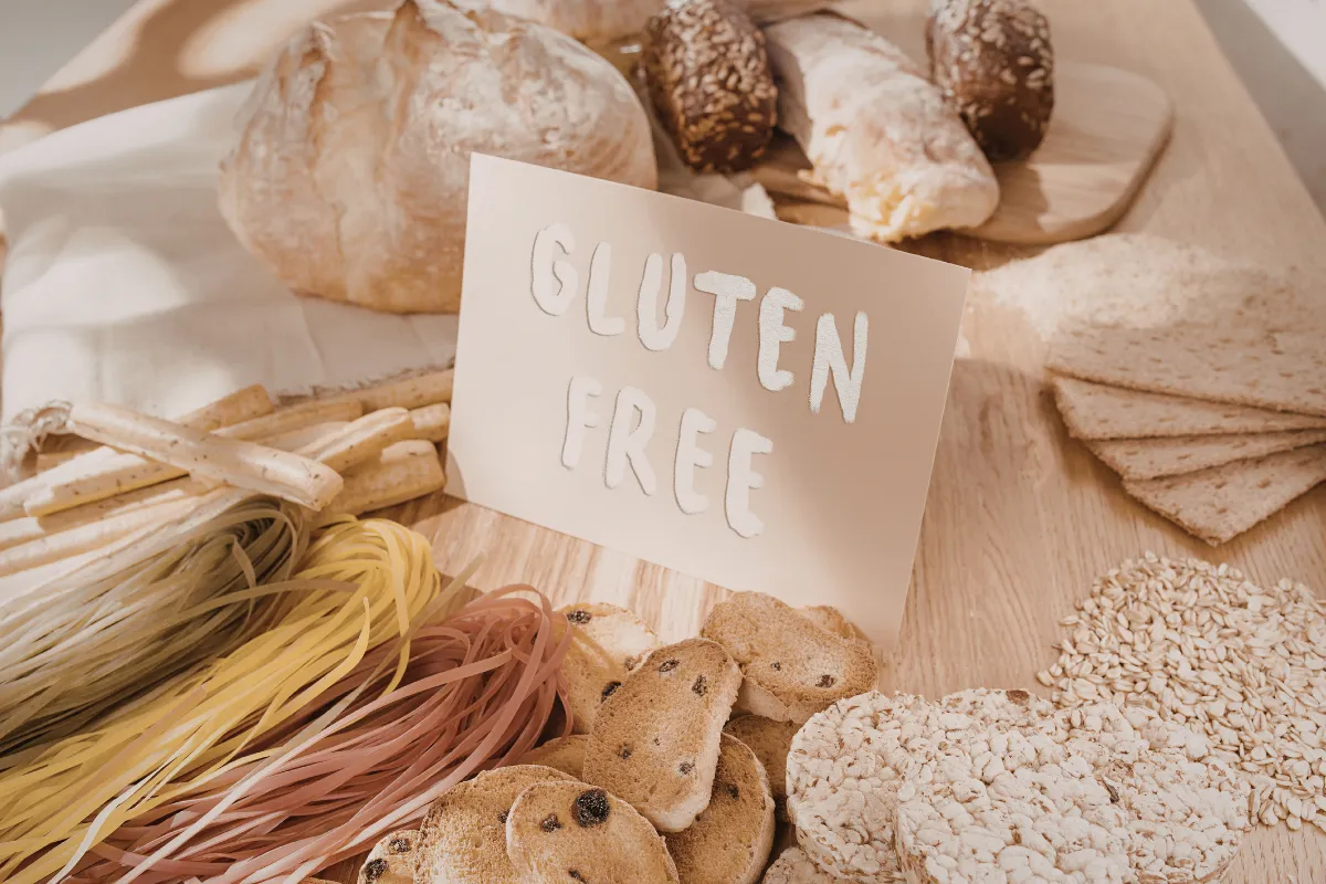 Un tavolo con pane, pasta, biscotti e cereali disposti intorno a un cartello con la scritta "senza glutine".