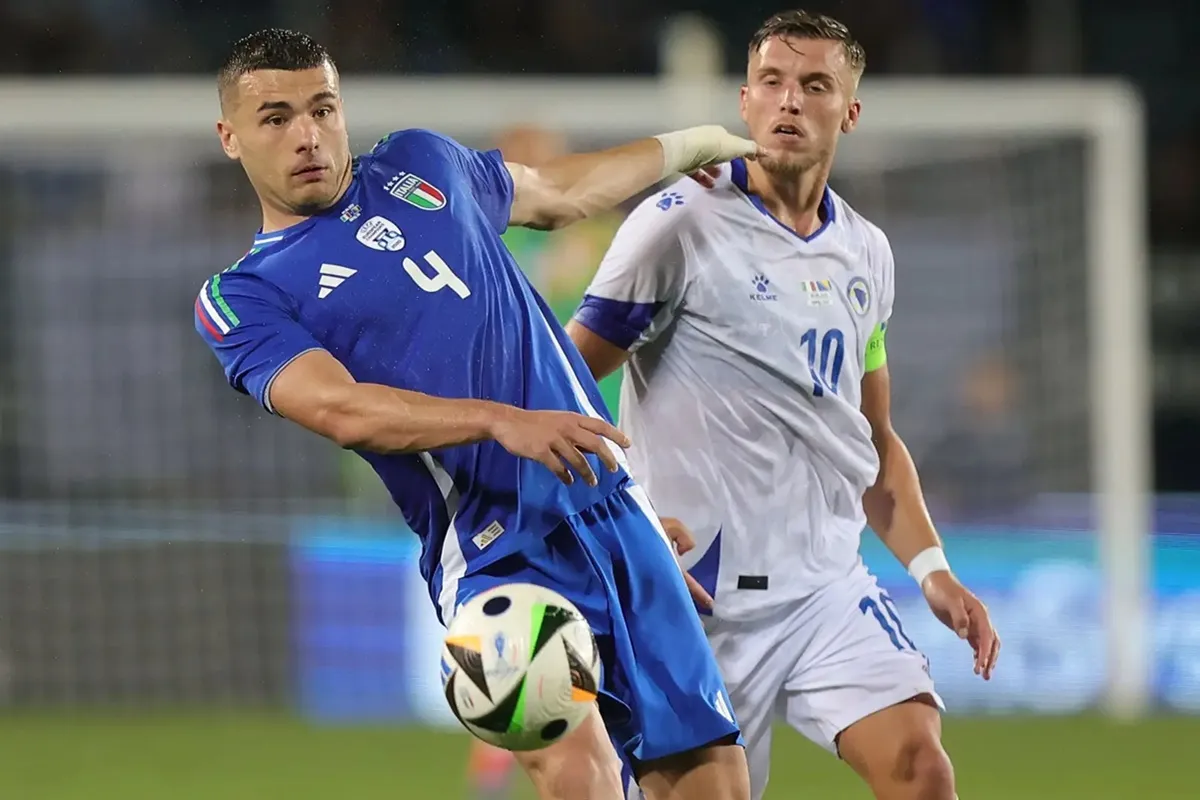 Giocatore della nazionale italiana in maglia blu controlla il pallone durante una partita contro la Bosnia con un avversario vicino