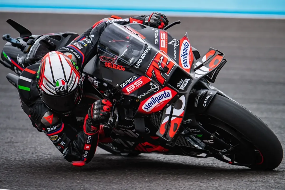 Pilota MotoGP inclinato al massimo in curva su una moto Aprilia nera e rossa durante una gara