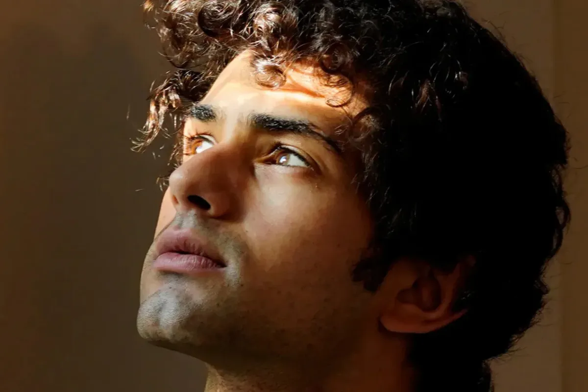 Un giovane con i capelli ricci guarda verso l'alto con un'espressione pensierosa.