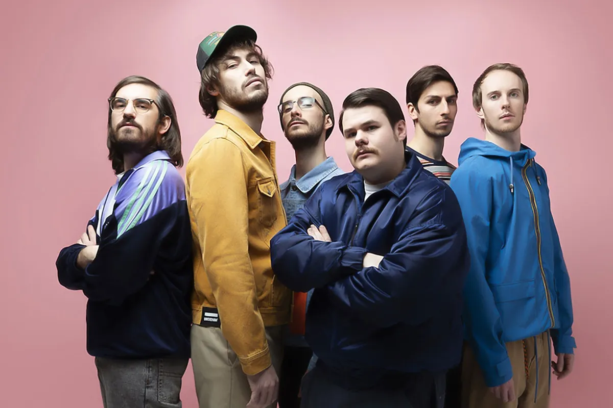 Membri della band italiana Pinguini Tattici Nucleari posano insieme davanti a uno sfondo rosa per una foto promozionale