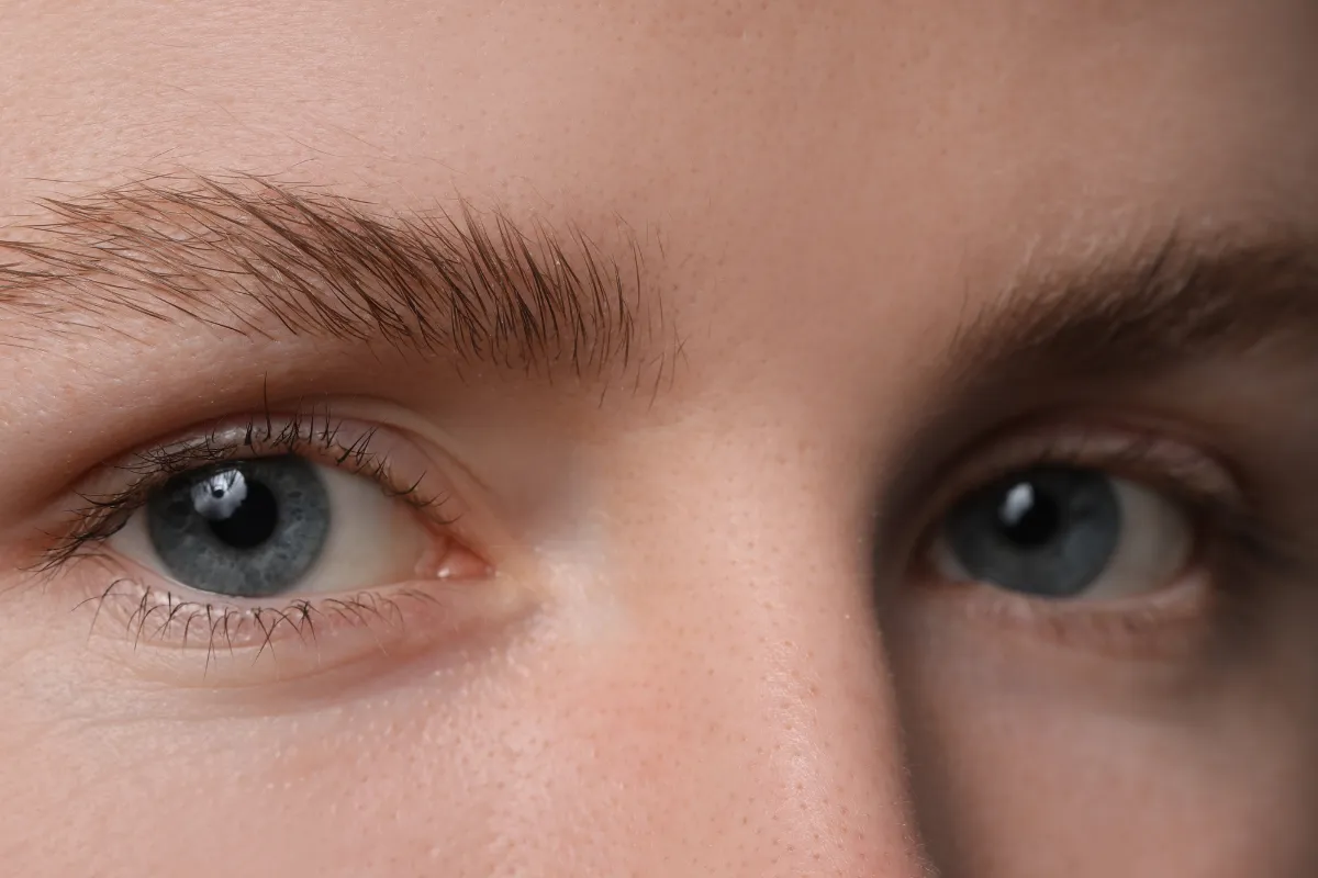 Primo piano di un viso con occhi chiari e sopracciglia naturalmente folte.