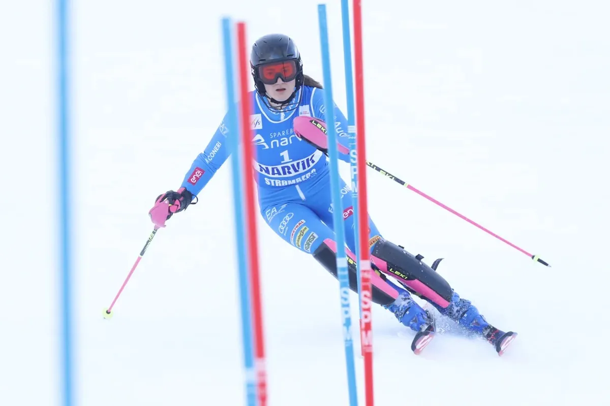 Sciatrice alpina con tuta blu e casco attraversa i pali rossi e blu durante una gara di slalom sulla neve