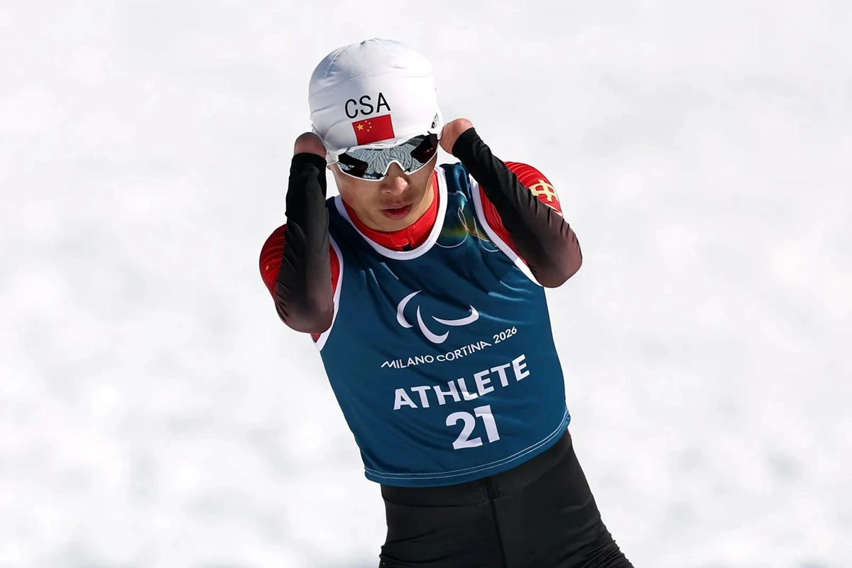 Atleta paralimpico cinese con pettorale Milano Cortina 2026 e casco CSA mentre gareggia sulla neve durante una competizione sportiva