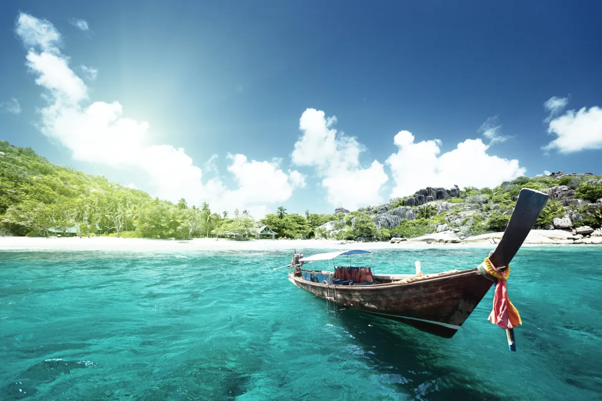 Una barca di legno ancorata in acque turchesi vicino a una spiaggia circondata da vegetazione e formazioni rocciose sotto un cielo limpido.