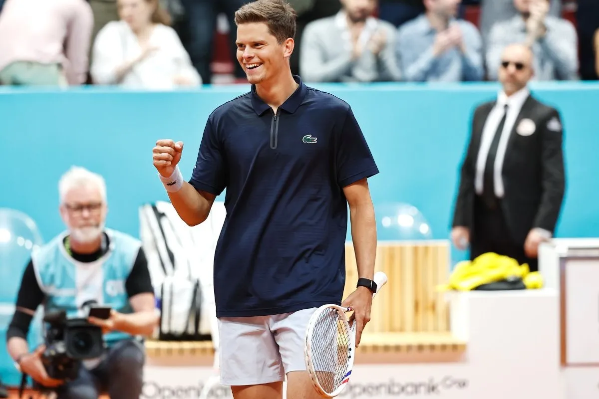 Tennista maschile sorride ed esulta durante un match su campo in terra battuta con racchetta in mano