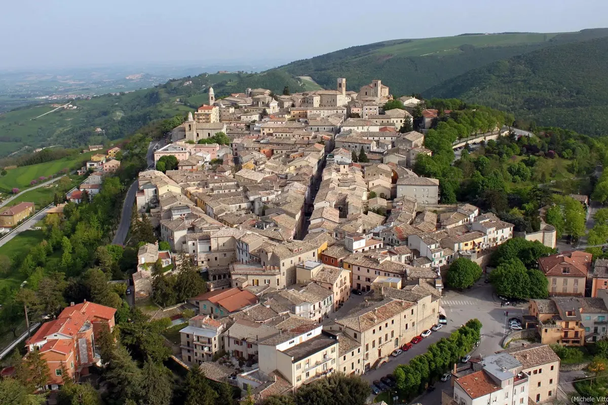 Veduta aerea di un borgo medievale italiano con case in pietra e tetti chiari circondato da colline verdi