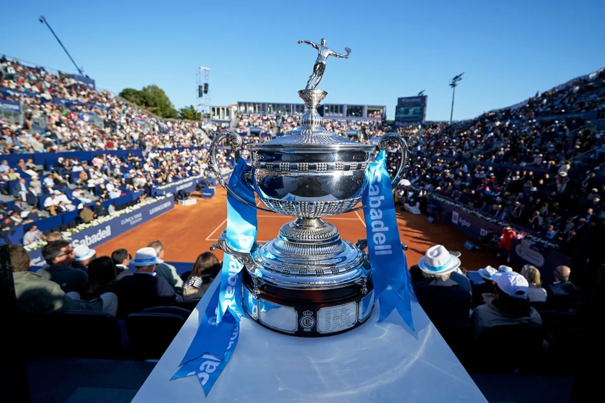 Trofeo di tennis esposto su campo in terra battuta con pubblico sugli spalti durante un torneo