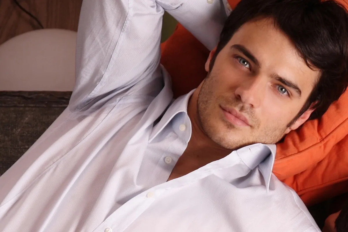 Uomo con occhi chiari sdraiato su divano arancione indossa camicia elegante azzurra