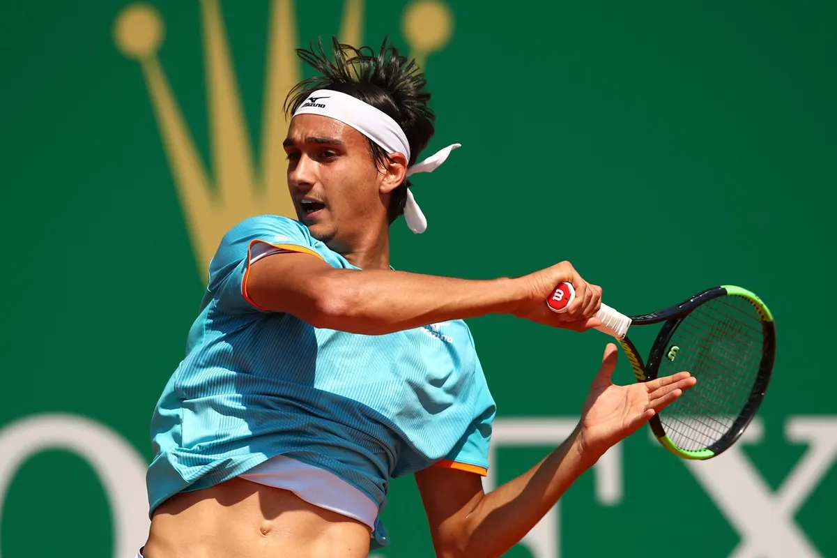 Tennista maschile esegue un colpo di dritto durante una partita su campo in terra con sfondo verde