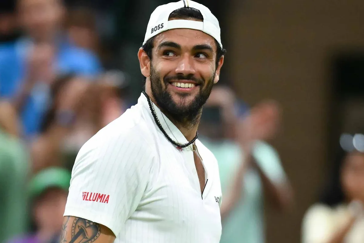 Tennista Matteo Berrettini con cappellino bianco sorride durante una partita su campo in erba