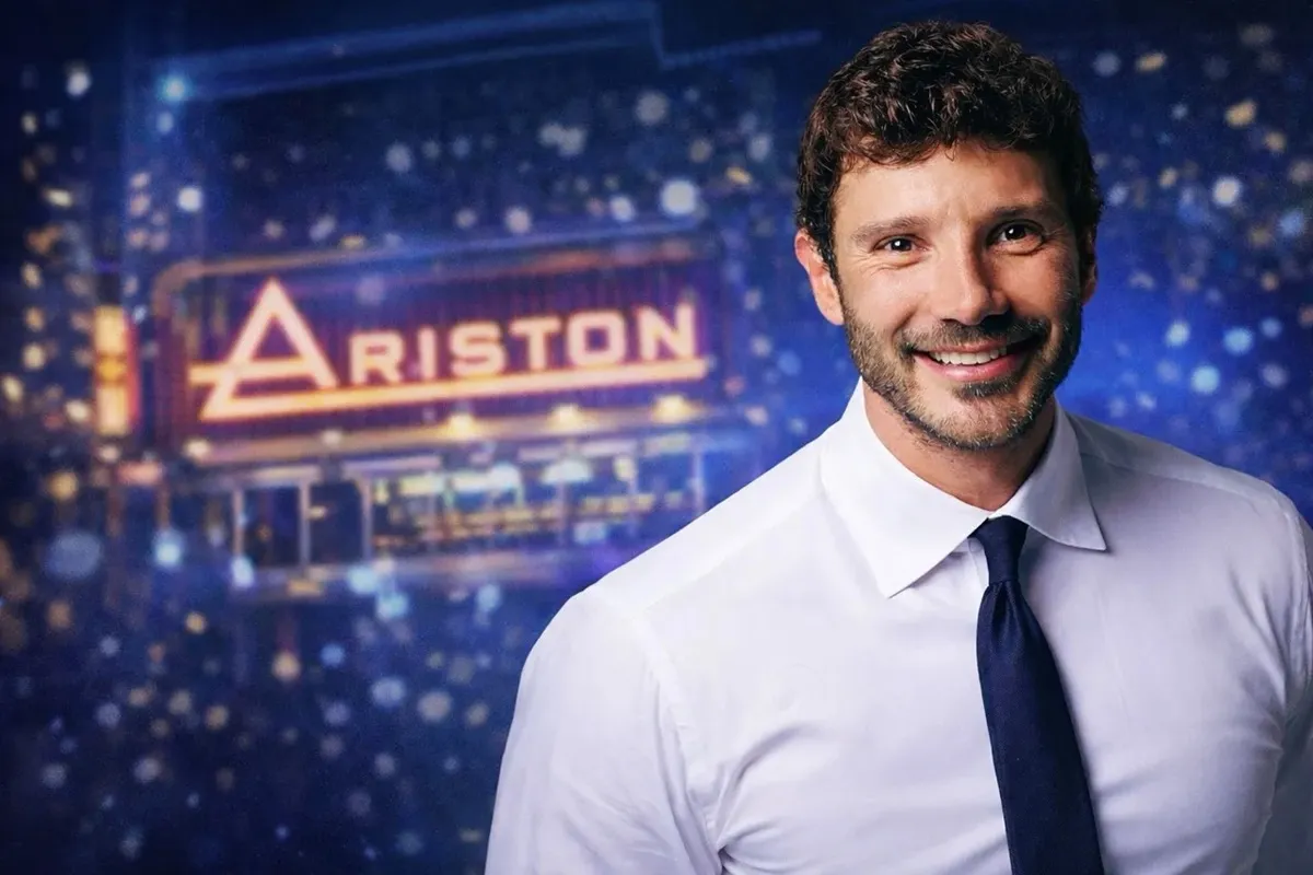 Uomo sorridente in giacca e cravatta davanti al Teatro Ariston illuminato durante il Festival di Sanremo