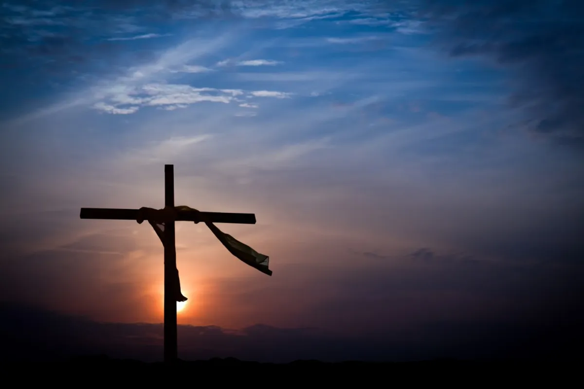 Silhouette della croce con Gesù crocifisso al tramonto, cielo colorato e atmosfera religiosa del Venerdì Santo