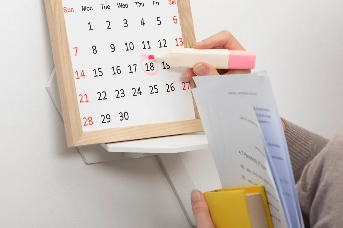 Mano che evidenzia una data sul calendario scolastico mentre tiene documenti e libri