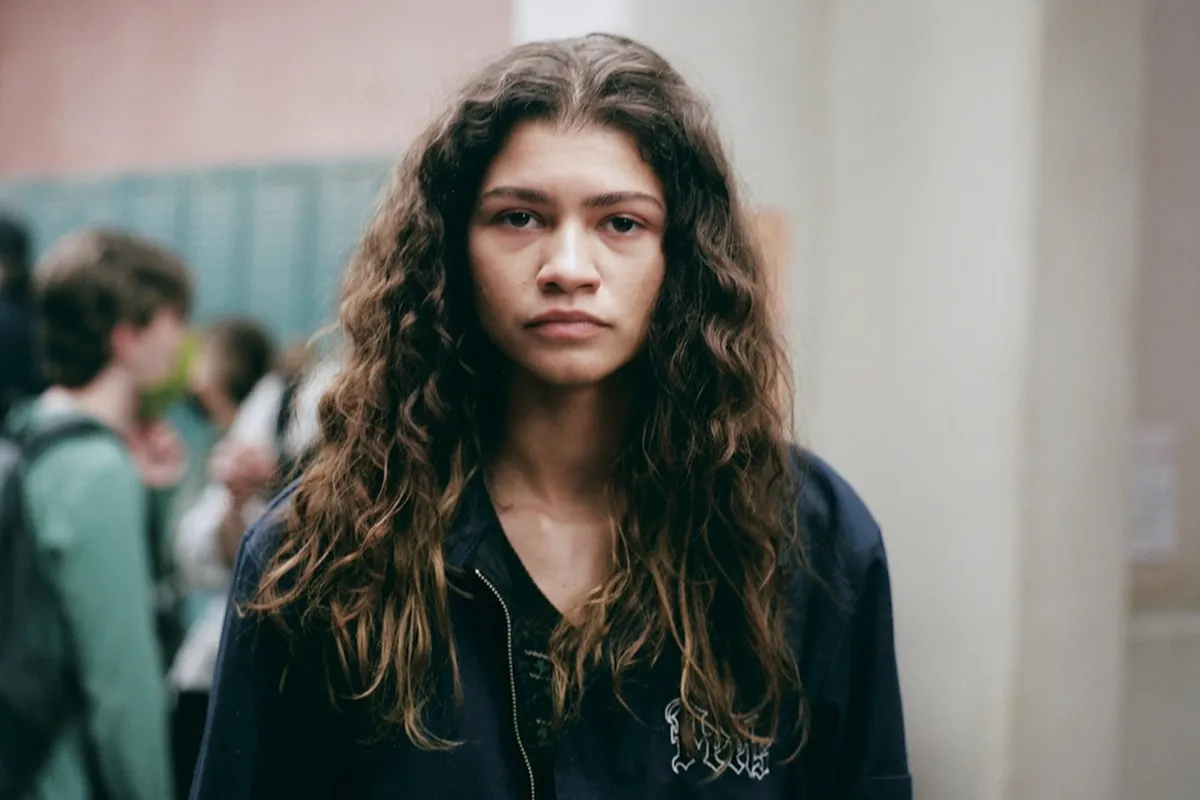 Ragazza adolescente con capelli lunghi e ricci che guarda frontalmente con espressione seria in un corridoio scolastico