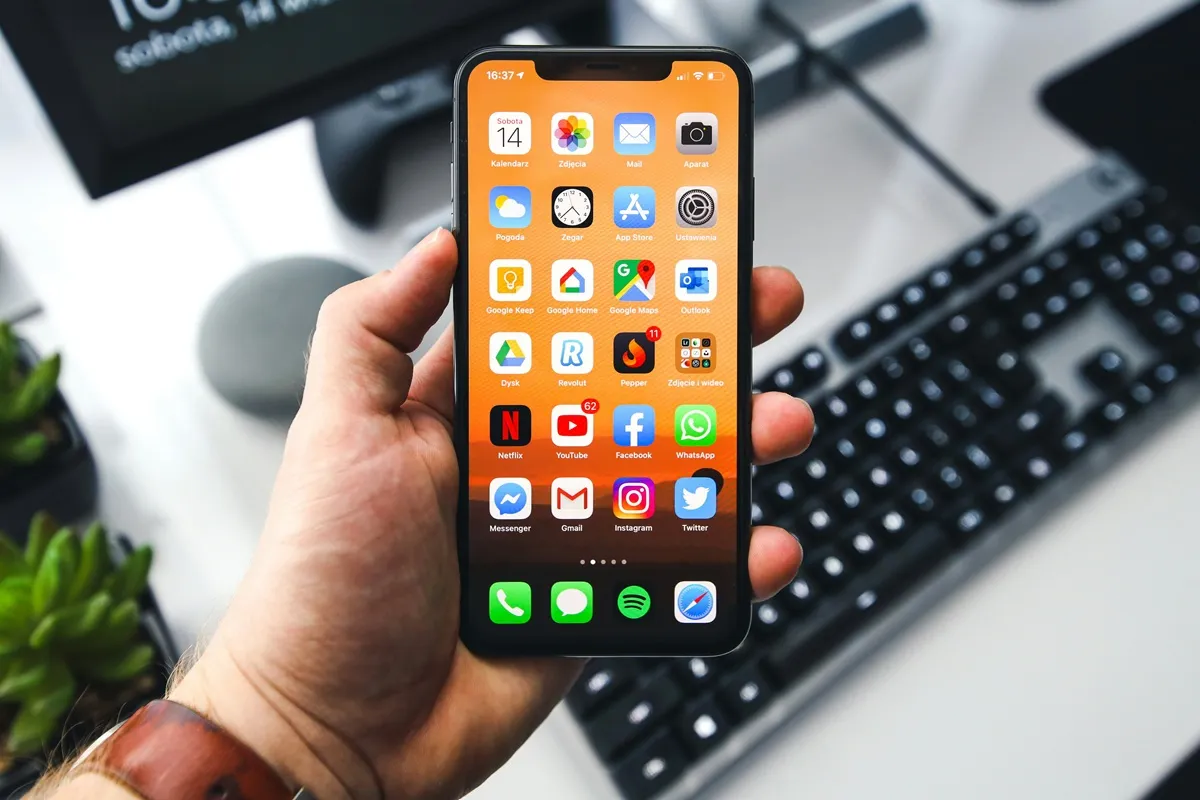 Mano che tiene uno smartphone con schermata iOS piena di app social davanti a una tastiera