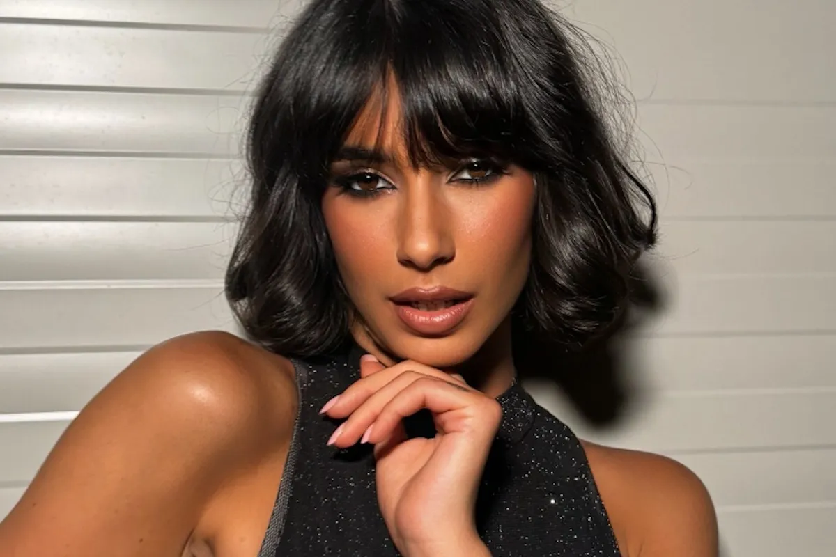 Donna con capelli scuri taglio bob e frangia, trucco elegante e posa sensuale con mano sotto il mento