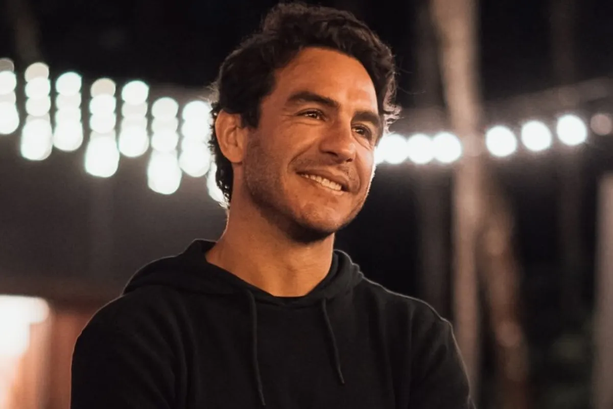 Uomo sorridente con felpa nera in un ambiente notturno illuminato da luci decorative sfocate